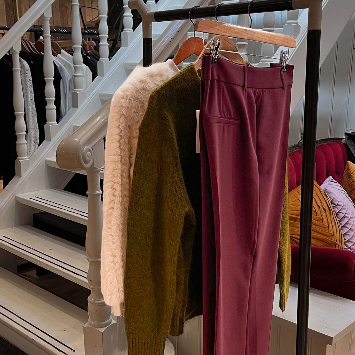 Faux fur, een grove knit en een bordeauxrode pantalon naast elkaar aan het rek